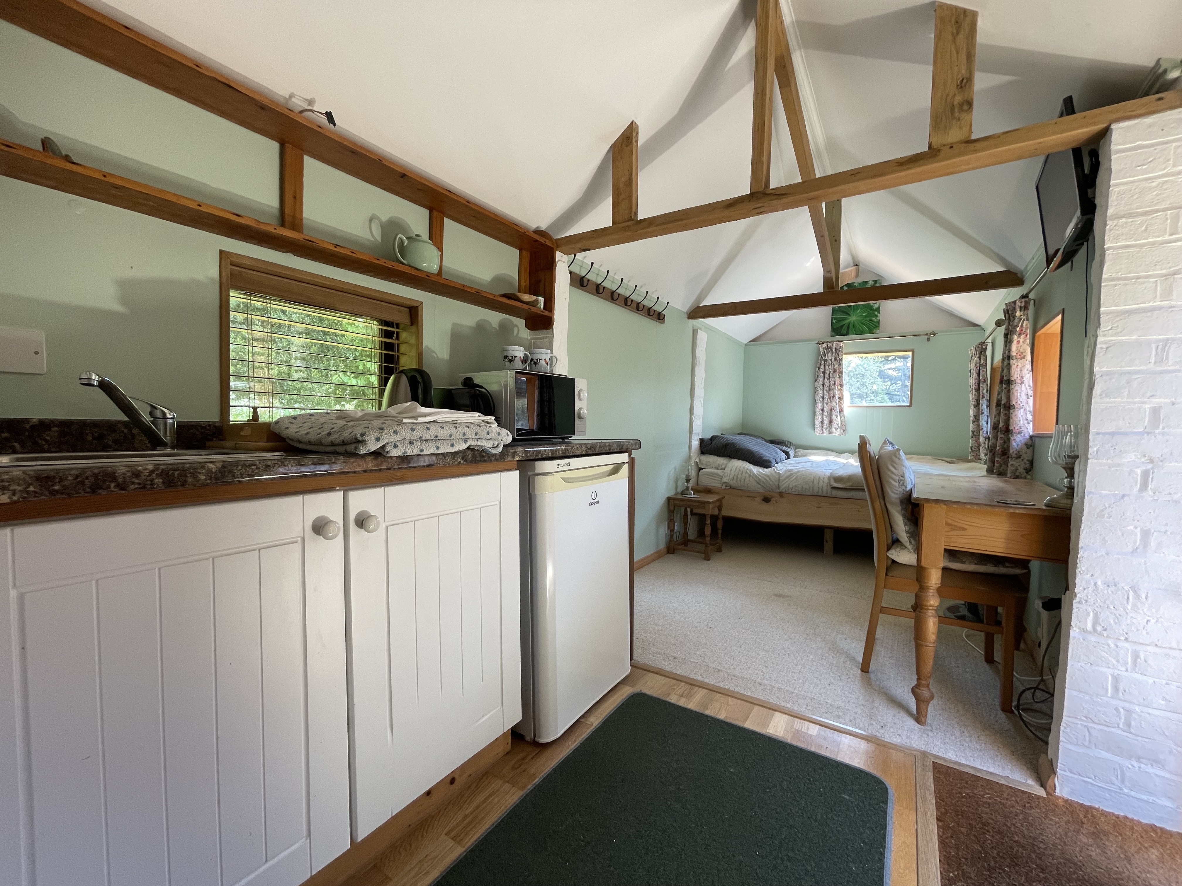Interior of the existing cottage showing exposed beams, kitchenette and cosy bedroom
